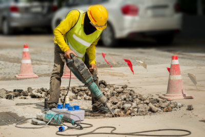 Worker drilling concrete driveway with jackhammer